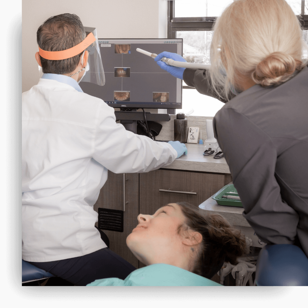A dentist and dental assistant reviewing digital X-rays on a computer monitor while a patient lies back in the dental chair.