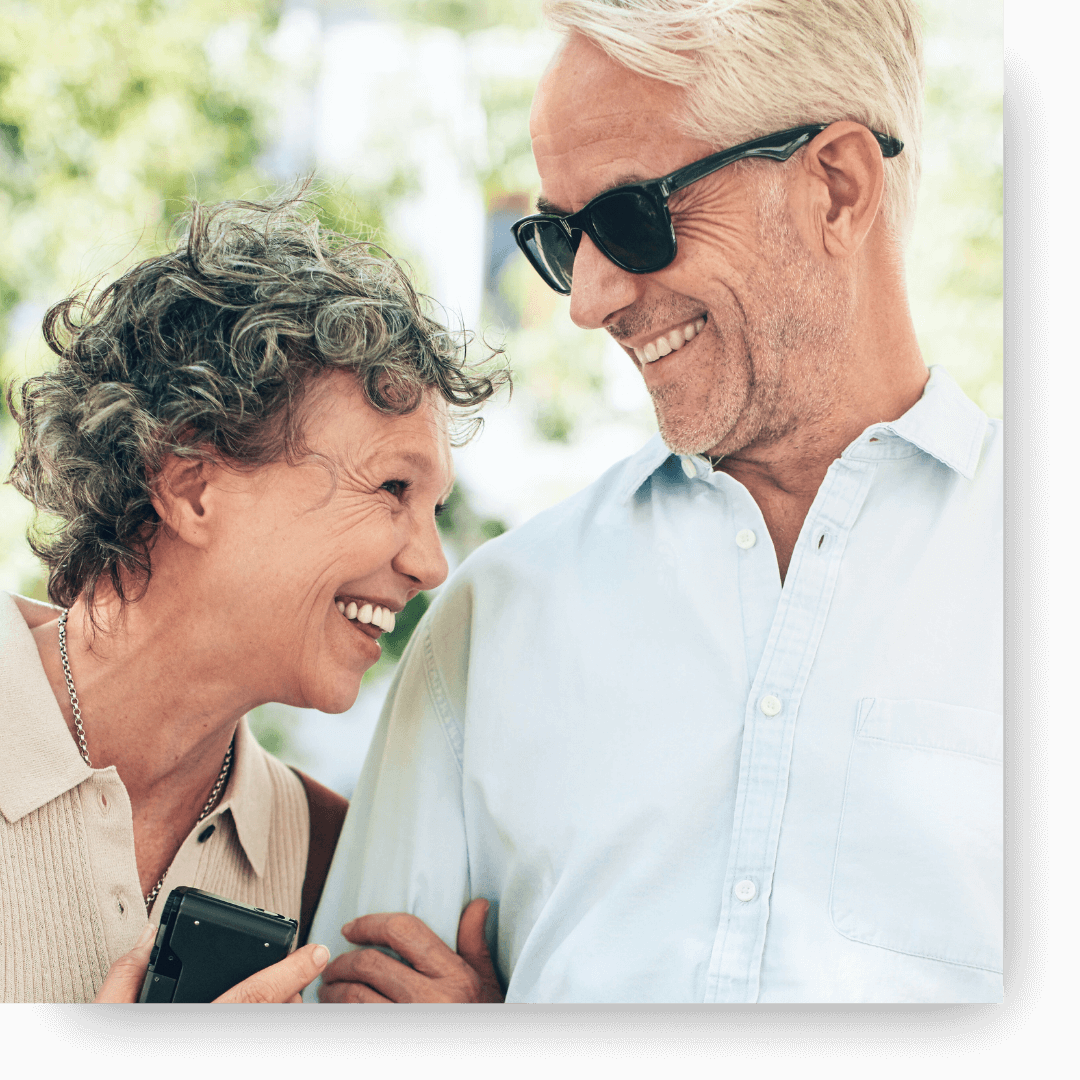 A happy senior couple smiling at each other outdoors, showcasing healthy smiles.